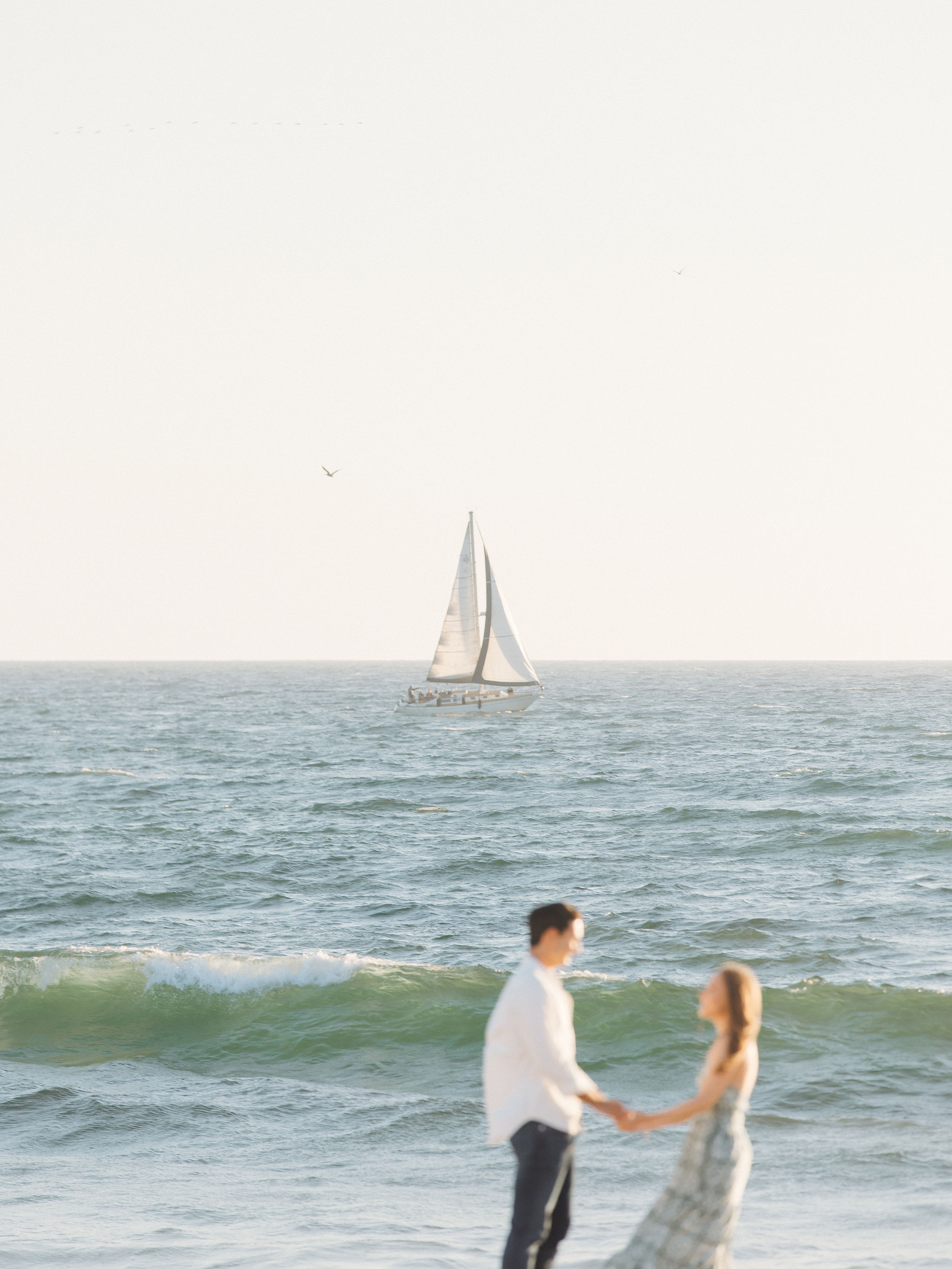 Couple at beach with sailboat at sunset