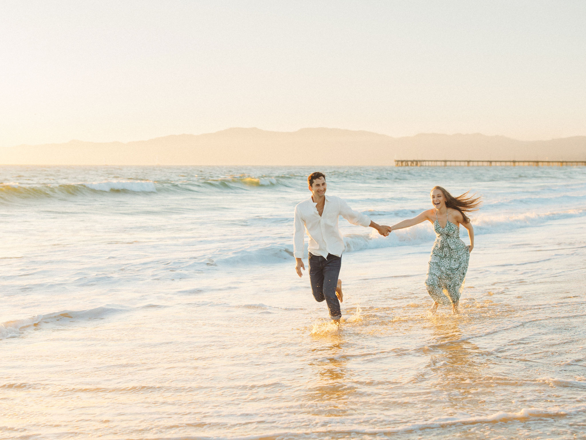 Couple running through waves at golden hour